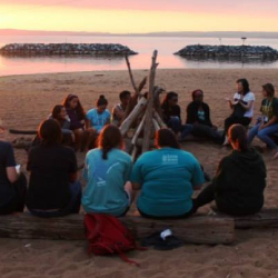 SEEDS students on a leadership retreat, sitting on the beach in a circle at sunset