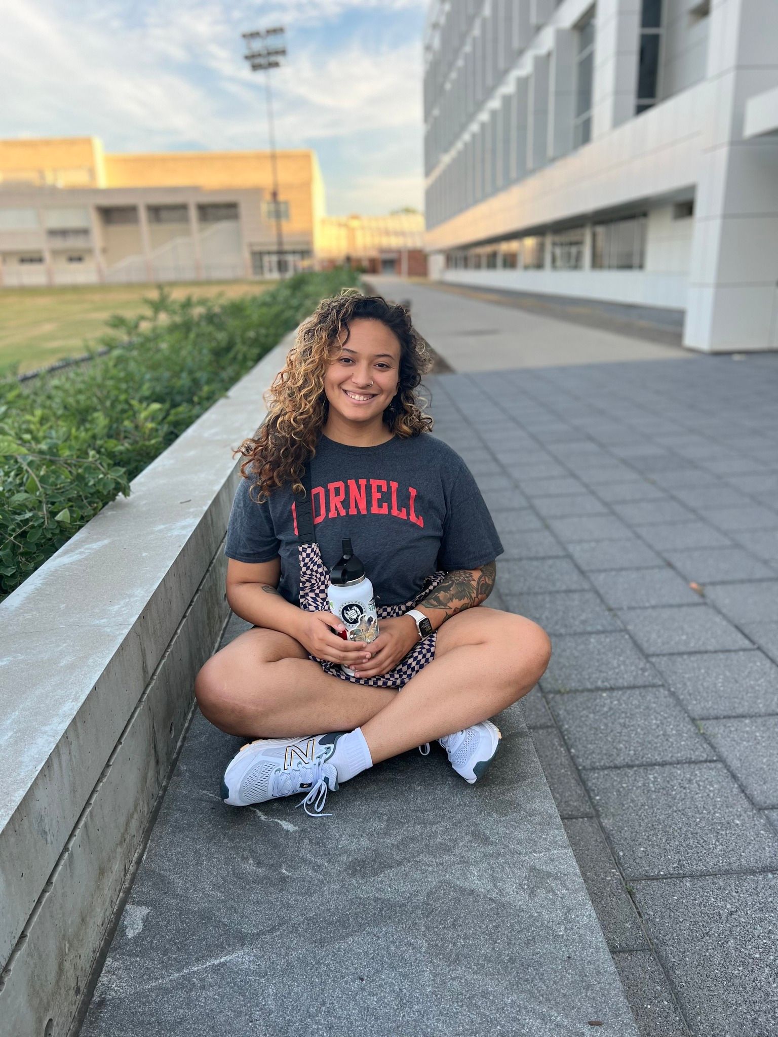 Photo of girl in Cornell t-shirt, cross legged, smiling at camera