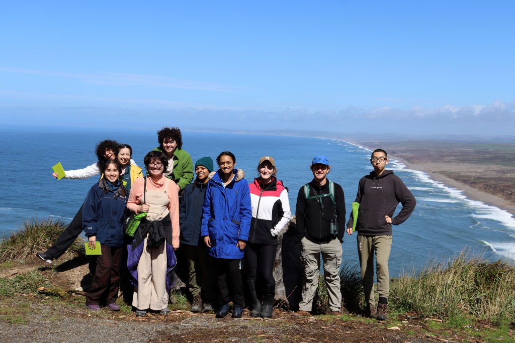 A row of participants pose near a cliff with the Pacific Ocean in the background.