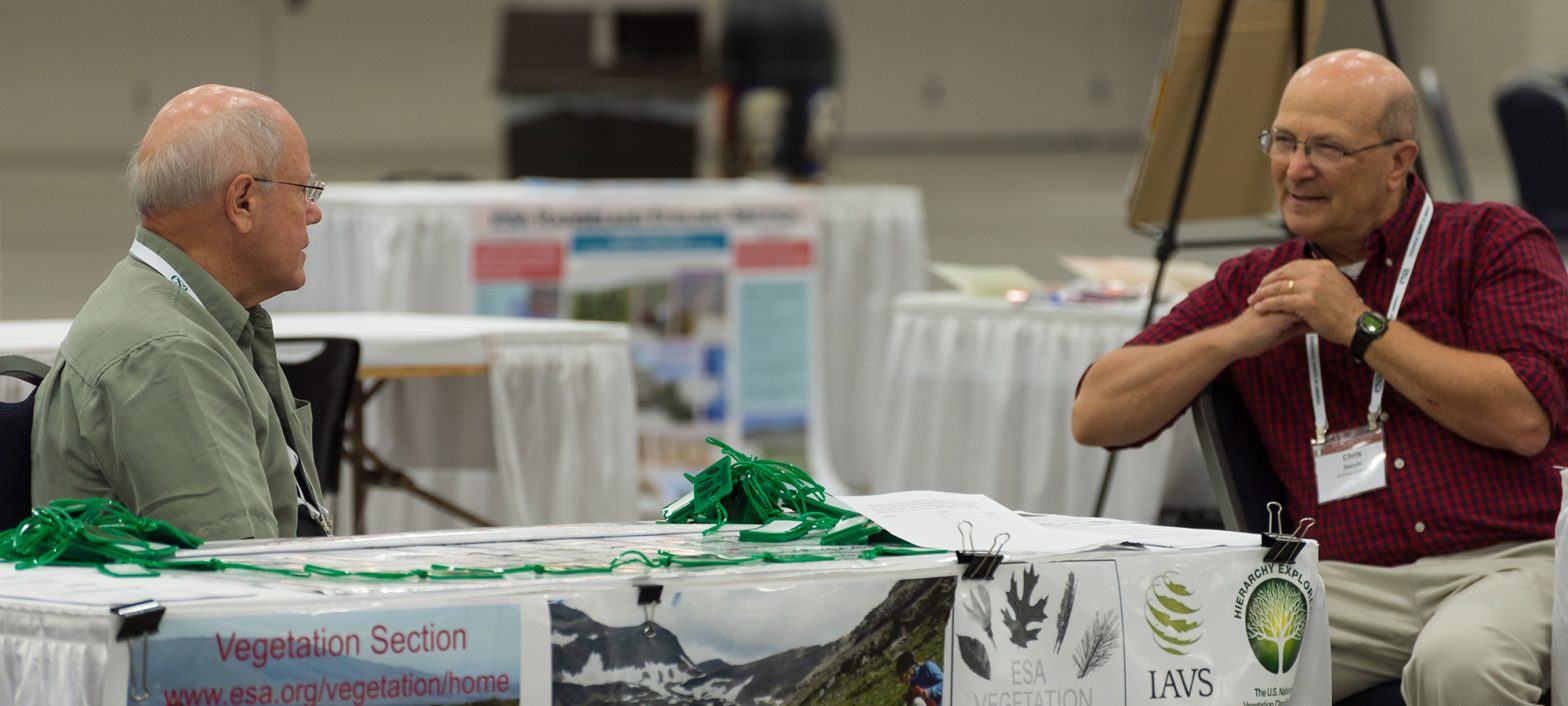 Two seated gentleman converse in the vegetation section booth at the 2019 Annual Meeting.