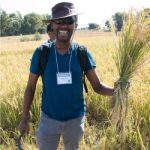 Certified ecologist Moffatt Ngugi smiles broadly with grain he harvested as part of his agroecology program