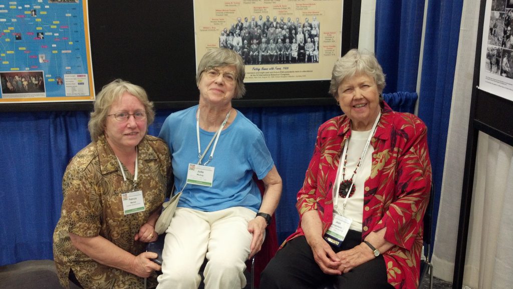 Three women attendees sit near an archival photo at the HRC booth.