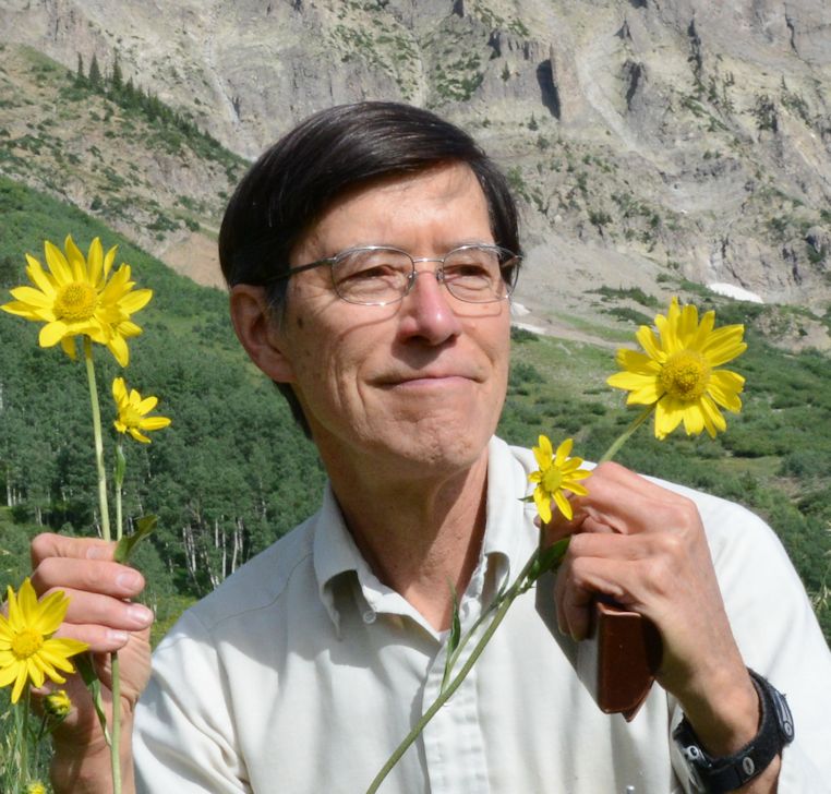 Portrait image of David Inouye holding some flowers with a mountainous backdrop.
