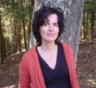 Portrait of Dr. Maria Uriarte in a red sweater, black blouse in front of a tree in a forest.