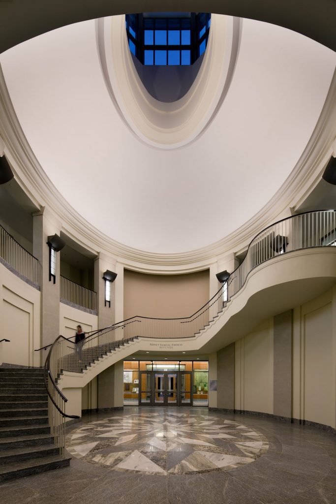 A large circular staircase winds up to an egg shaped white ceiling and glass roof. 