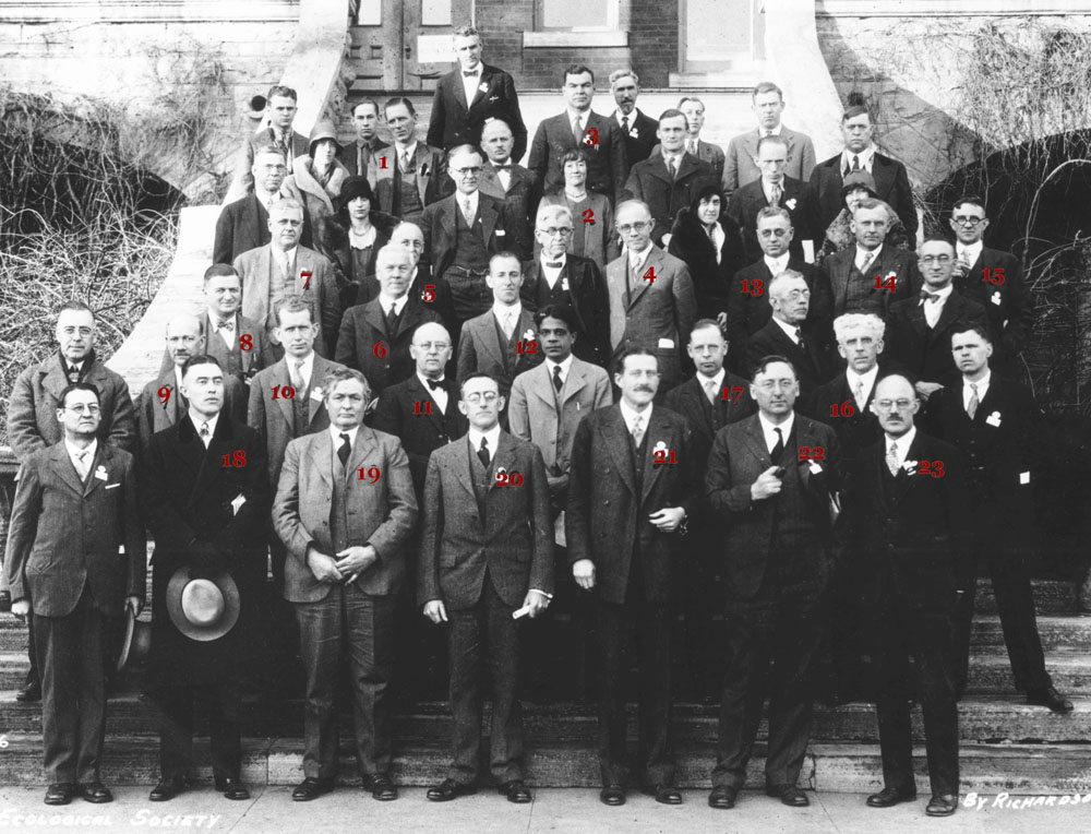 A black and white photo of roughly 30 ecologists dressed in coats and ties posing on a wide stairwell of a large building. There are approximately 5 women amongst all white men.