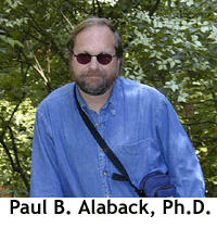 Portrait of Paul Alaback in a forest wearing sunglasses and a blue button down shirt.