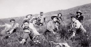 A group of people, presumably a teacher with her students, sit in an open field. Black and white, circa 1947.