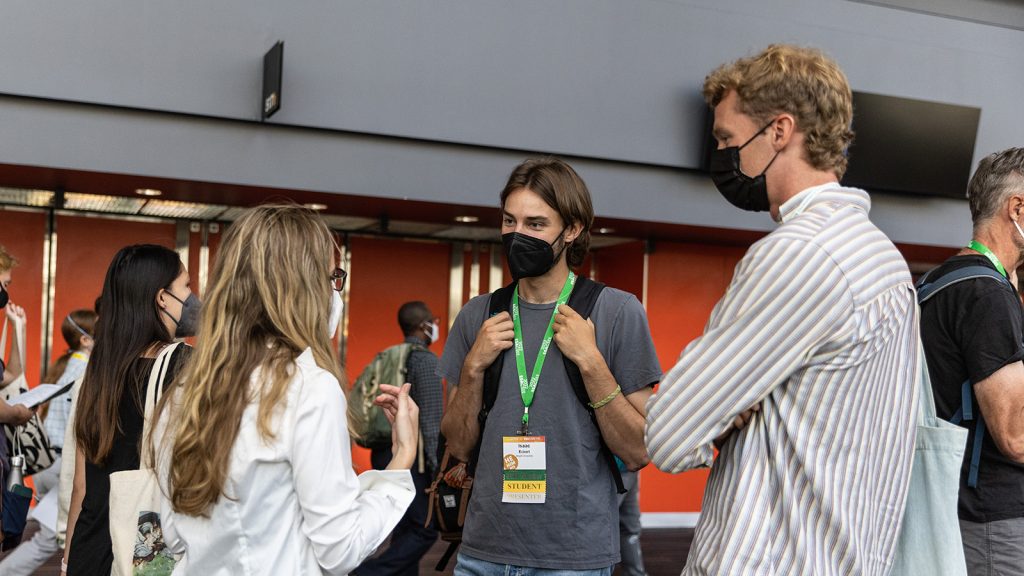 Three attendees discuss a topic outside a convention center room.