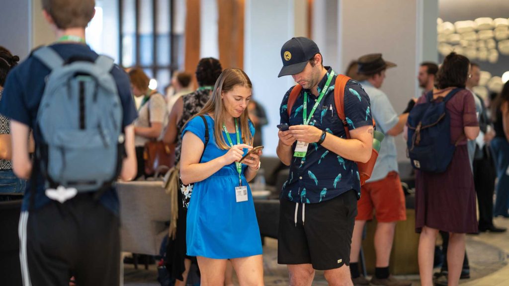 Two attendees stand together each looking at their own phone.