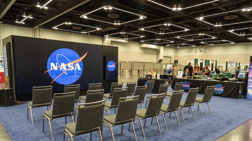 Representatives are seated along the National Aeronautics and Space Administration (NASA) booth at the ESA Annual Meeting.