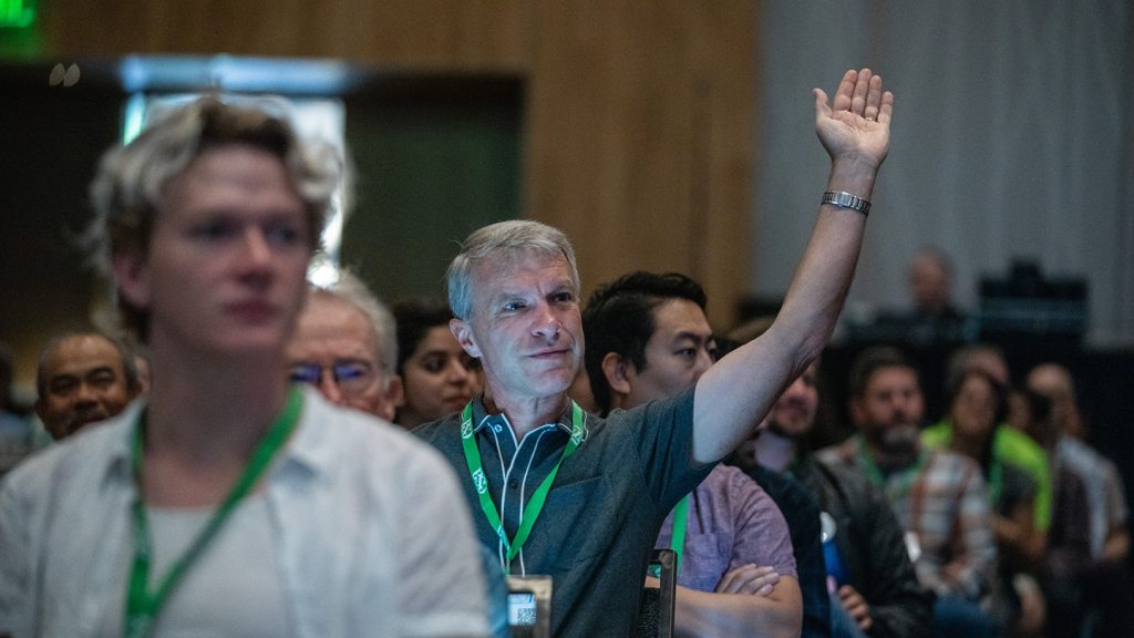 An attendee in the audience raises his hand. 