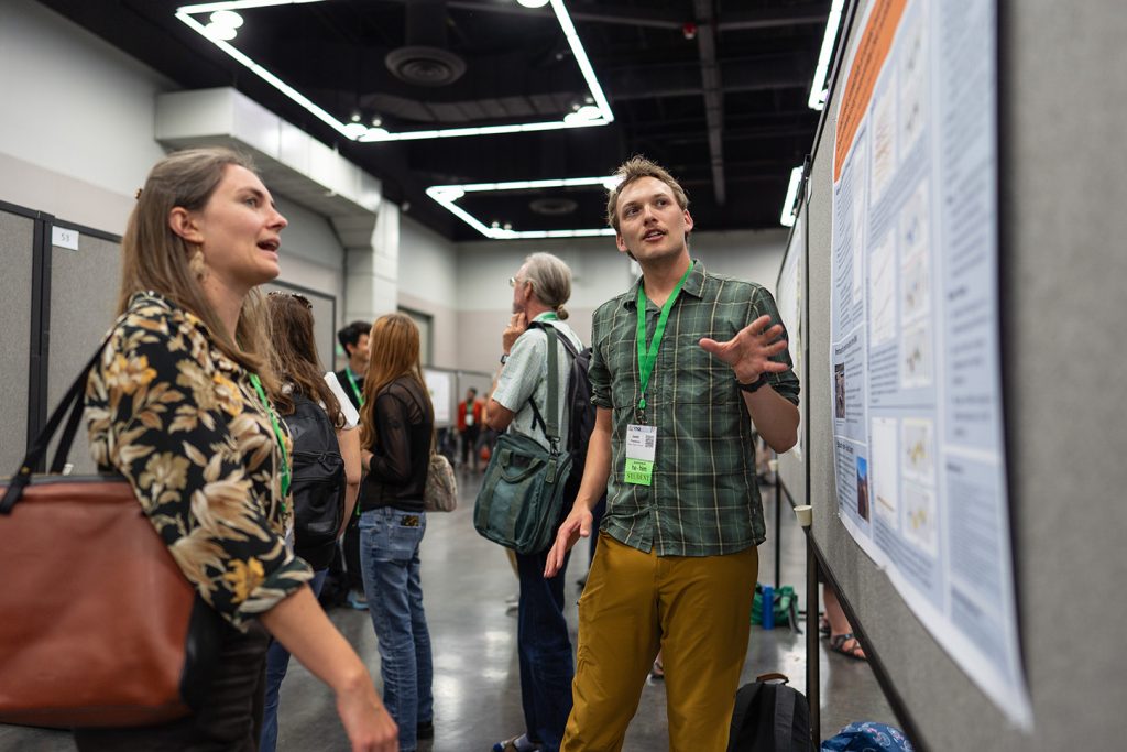 A poster presenter and watcher discuss a topic.