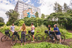 Five off road cyclists stop for break in front of a building with a graphic design on it.