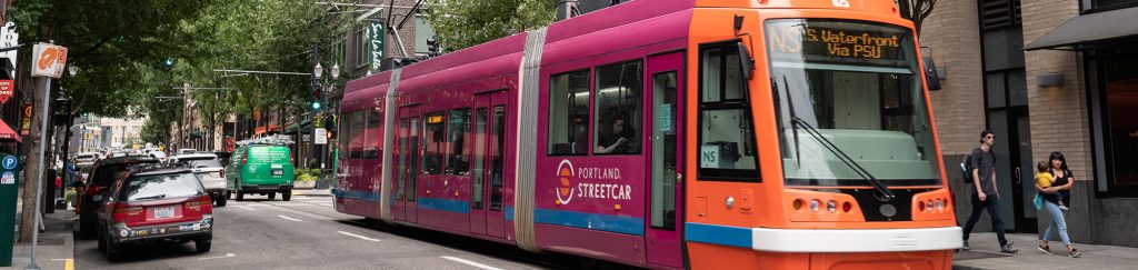 An orange and pink street car makes it way down the street.