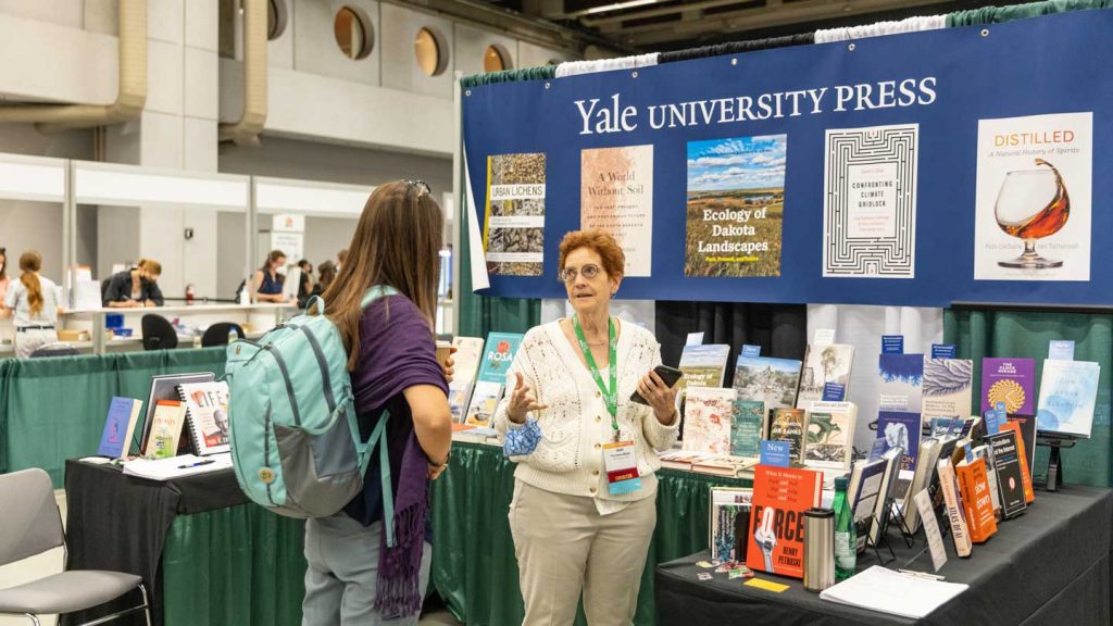 A woman at the Yale University press discusses something with an attendee.