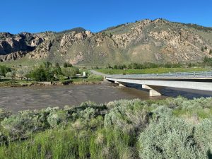 The sampling site on the Yellowstone River at Corwin Springs. Photo shows the Yellowstone River flowing under a bridge, with mountains in the background.