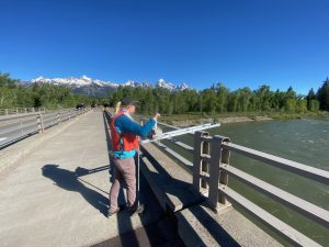 Ally standing on a bridge over the Snake River in Grand Teton National Park, using a bridge board and reel to collect samples from the water below.