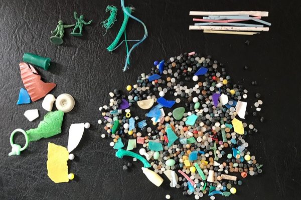 A cluster of small, colorful plastic pellets, broken shards, and small toys on a black leather surface. There is a 1-cent coin at the bottom of the photo for scale.