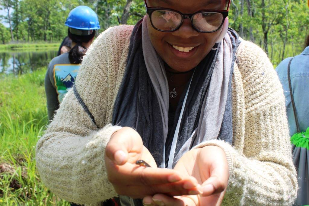 A student wearing glasses holds a small reptile in her hands.