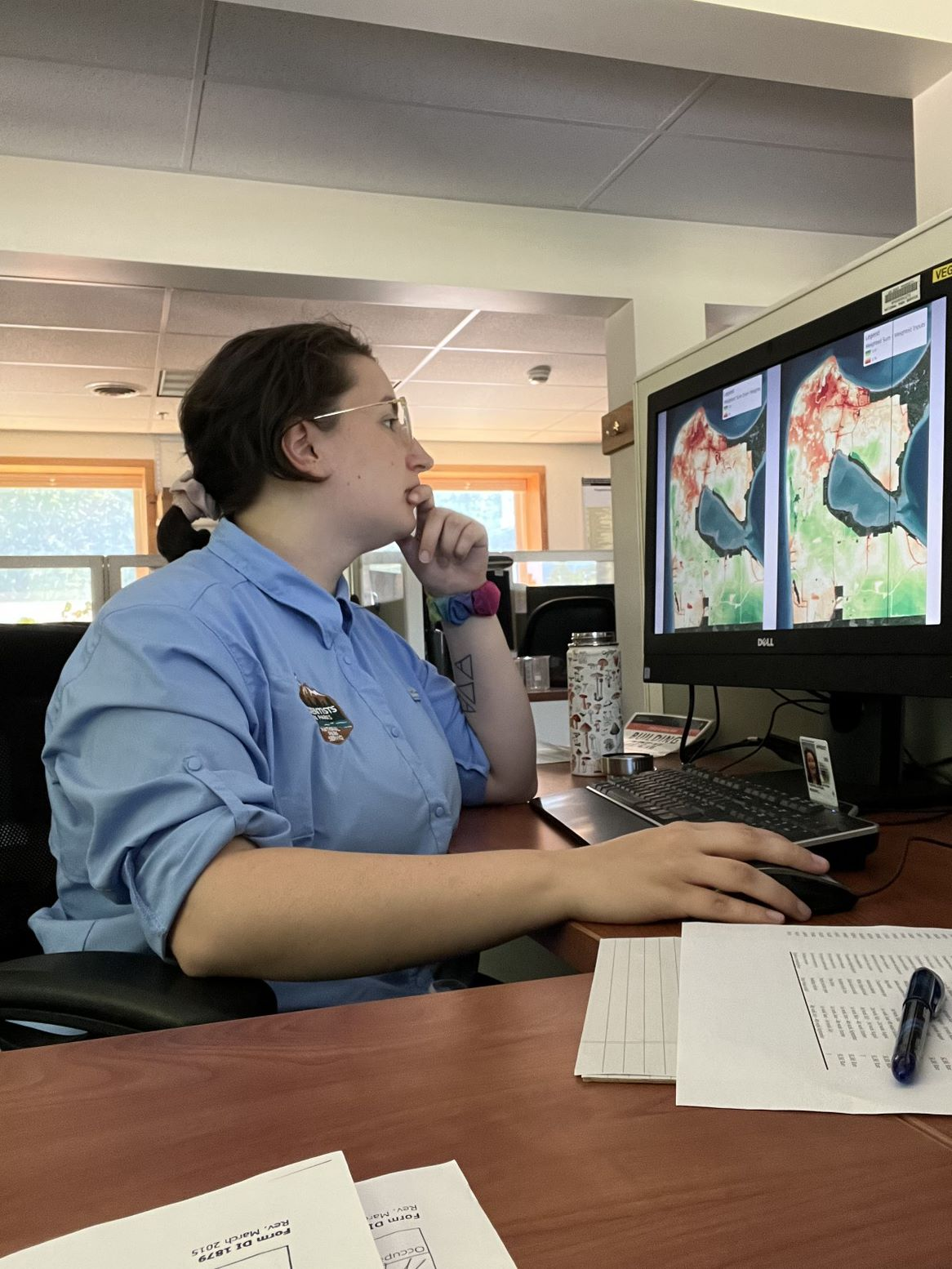 Student in glasses and a blue shirt sits in front of a computer. She edits maps in arcGIS.